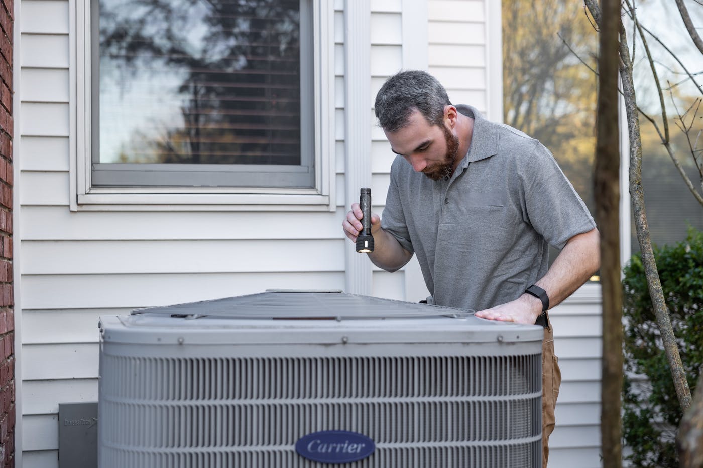 HVAC technician inspecting a residential Carrier condenser unit